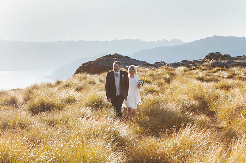 bride and groom walking through sun kissed grass on cecil peak