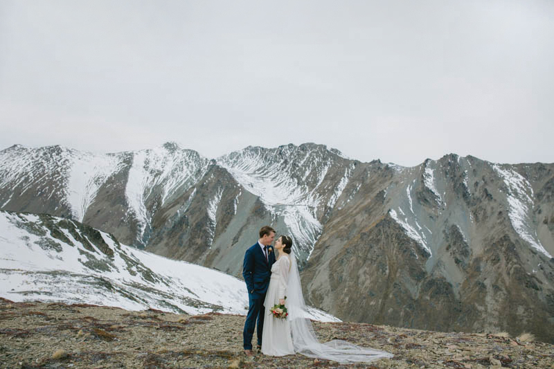 bride and groom on glacier with snowy mountain behind them
