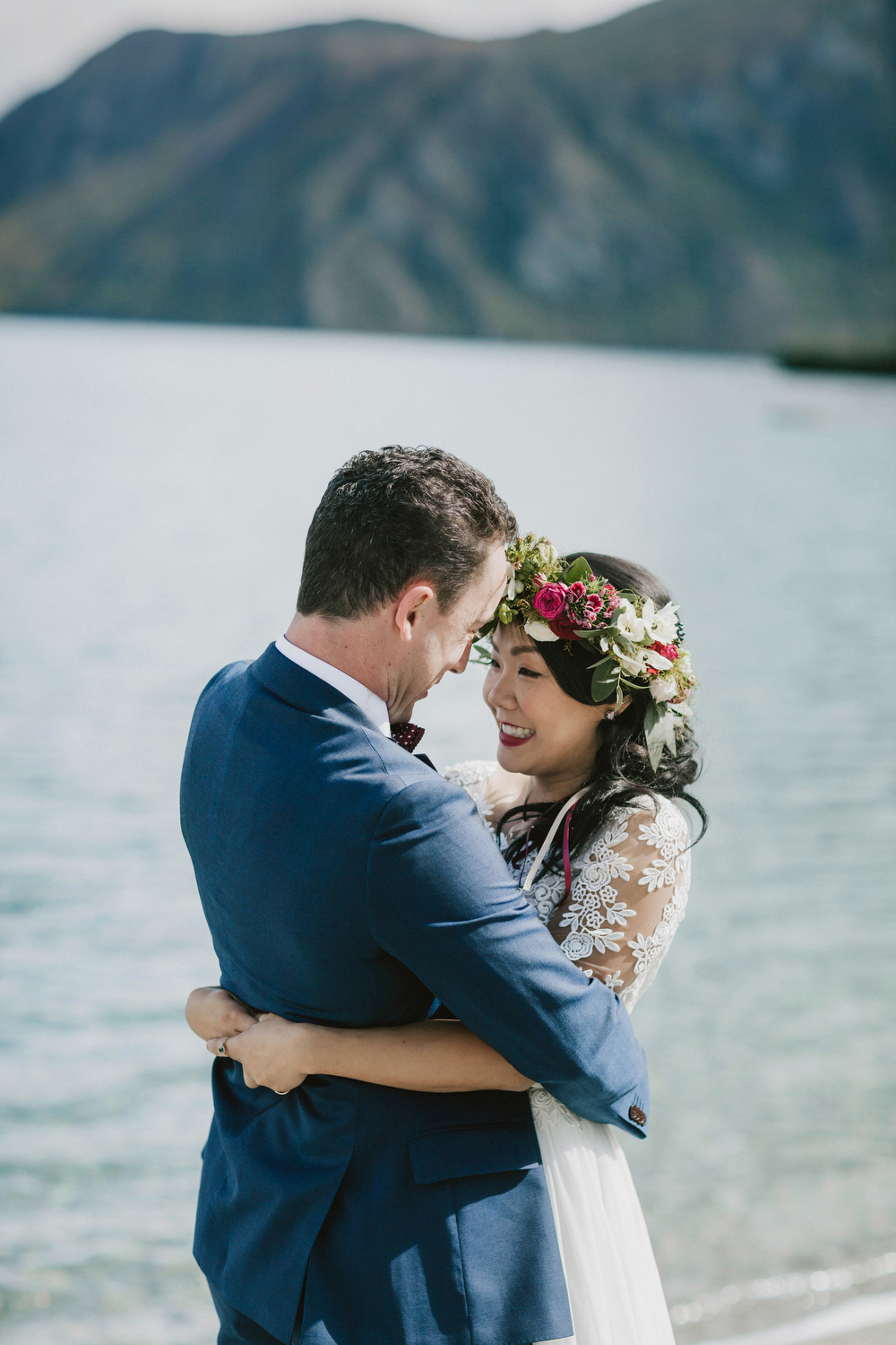 close up of bride and groom facing each other in front of lake