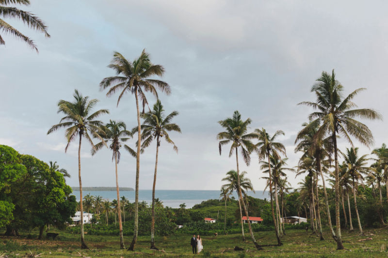 bride and groom in distance wide angle coconut plantation and ocean view
