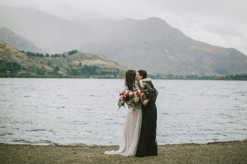 brides embracing in front of lake