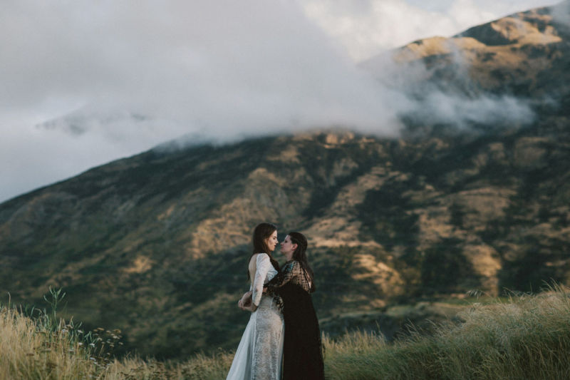 brides embracing with dramatic mountain behind them - facing each other
