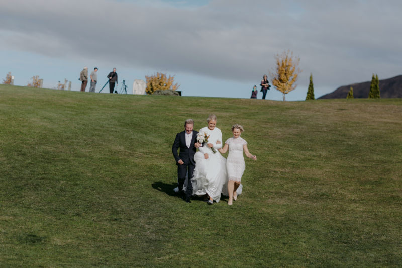 bride running down hill with mother and father