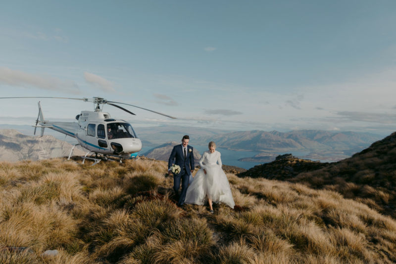 bride and groom on mountaintop walking away from heli