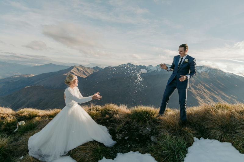bride and groom on mountaintop having a snow ball fight