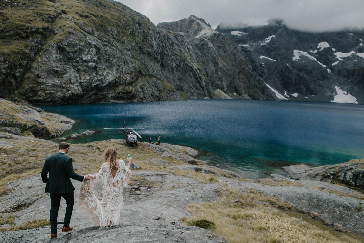 bride and groom walking towards lake with heli in background