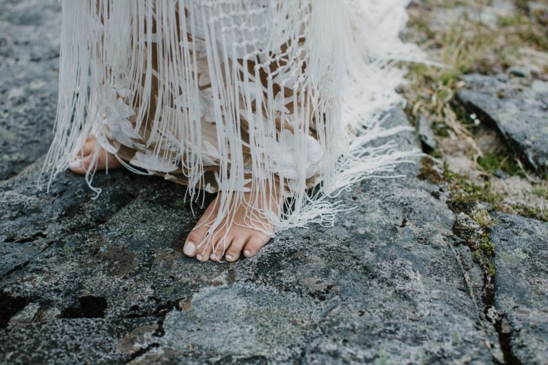 bride barefoot on rock with dress hanging down close up