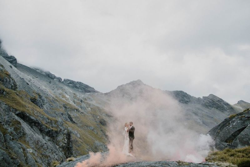 bride and groom in a cloud of pink smoke with mountains in the background