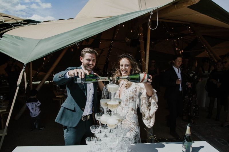 bride and groom happily filling champagne tower in tipi