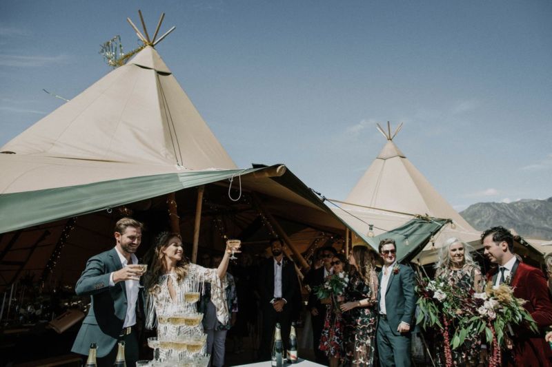 bride and groom cheers to the guests from the tipi with champagne glasses