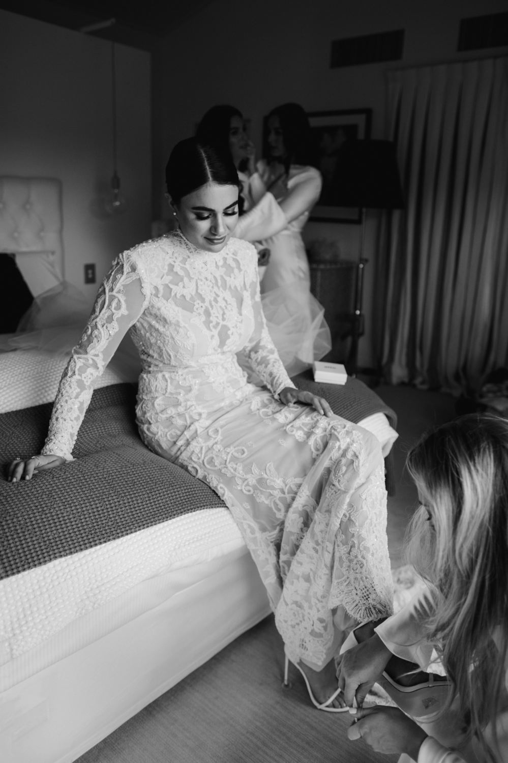 bride sitting on bed having her shoes put on