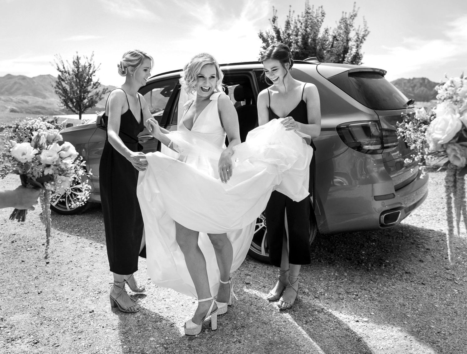bride stepping out of wedding car helped by her bridesmaids with dress held high