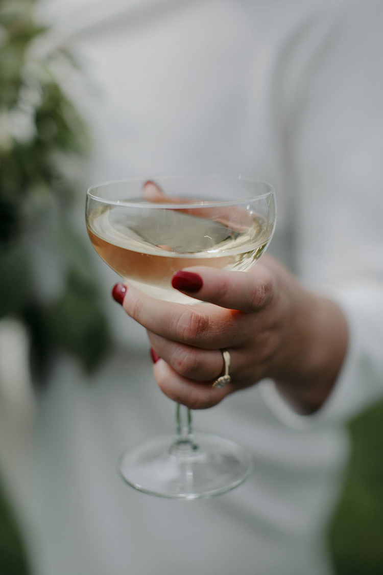 close up of champagne glass in brides hand showing bright red nail polish and her wedding ring