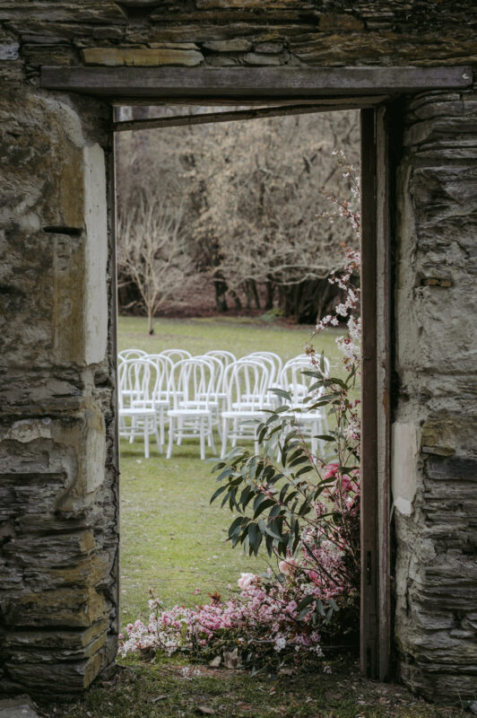 A peak through the Thurlby Domain ruins with ceremony chairs and pink floral arrangement decor
