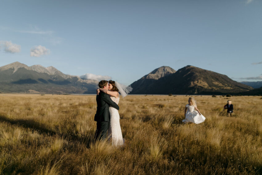 Bride and Groom kissing in field with children running up to them