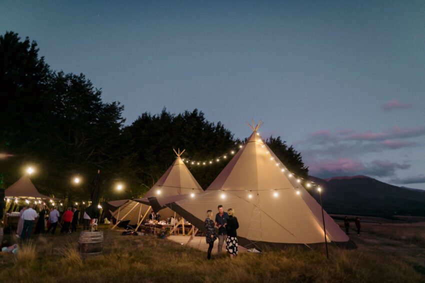 Candid of guests mingling outside tipi at night with festoon lights