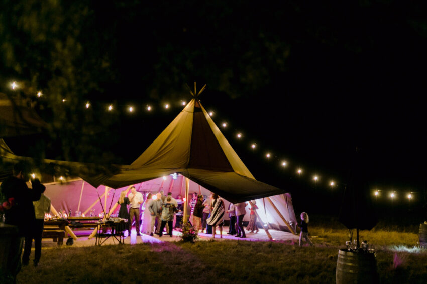 Candid of guests mingling outside tipi at night