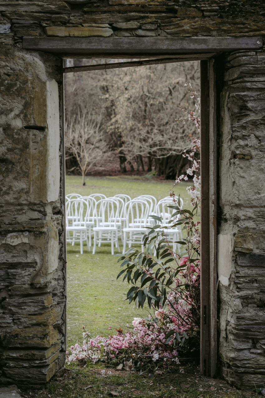 A peak through the Thurlby Domain ruins with ceremony chairs and pink floral arrangement decor