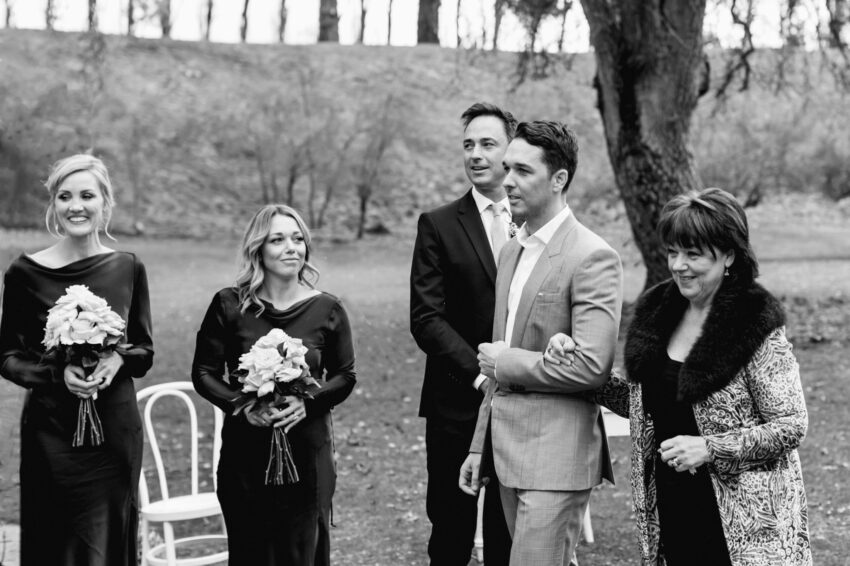 Groom and his mum walk past bridesmaid and bridesman