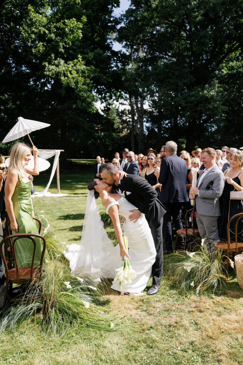 Bride and groom sharing a dip kiss as newlyweds hald way down the aisle