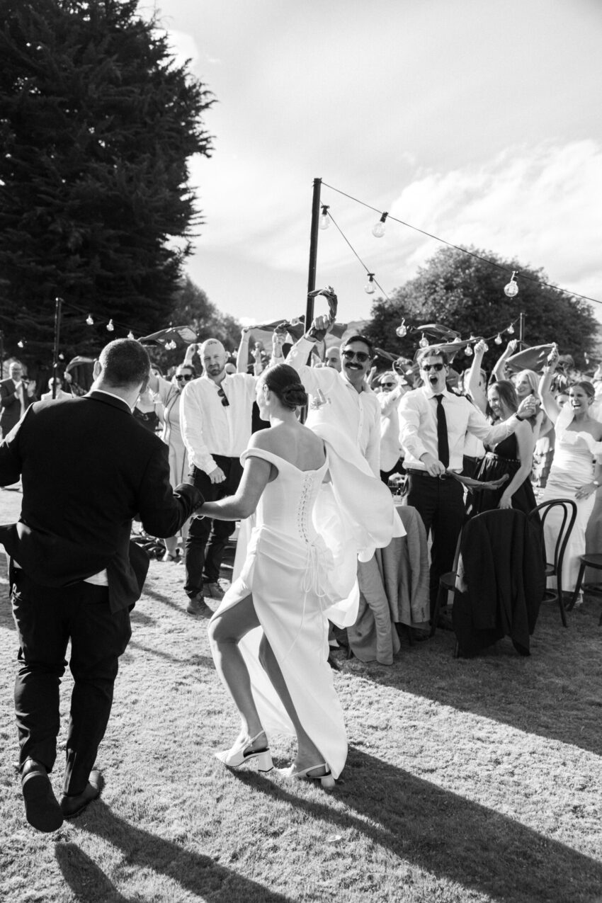 Bride and Groom run into their reception tables while guests all cheer and hold their napkins in the air