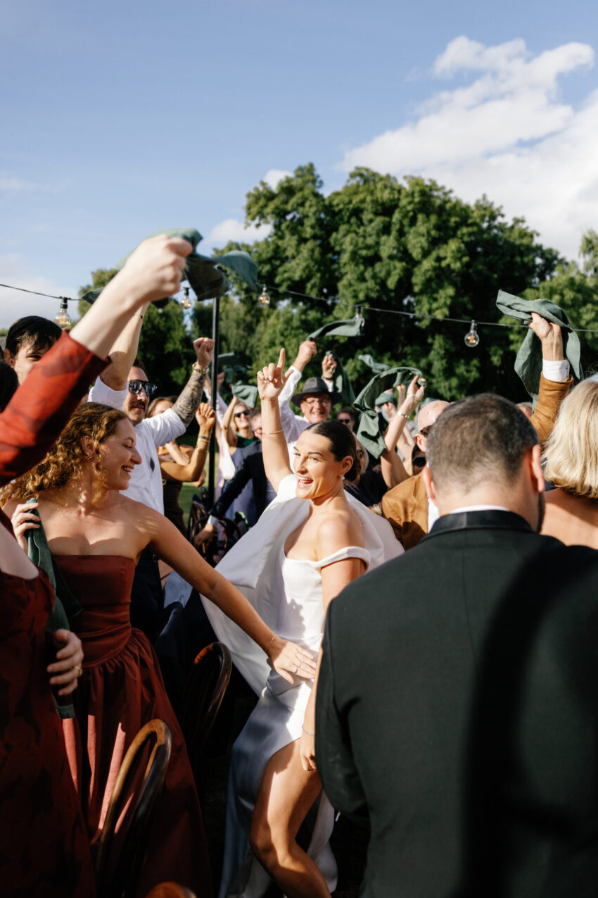 In the midst of the action, the bride runs into the middle of the reception tables while guests all cheer and hold their napkins in the air