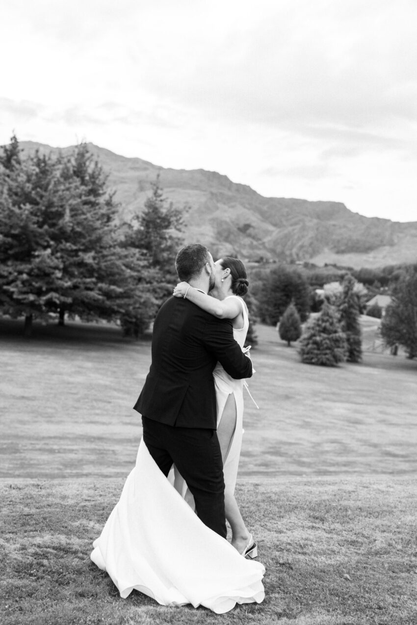 B&W portait of the bride and groom cuddling in front of a scenic backdrop