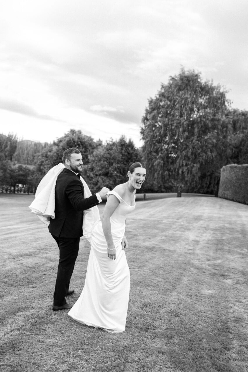 B&W of Groom carrying the end of the Brides dress and the Bride laughing