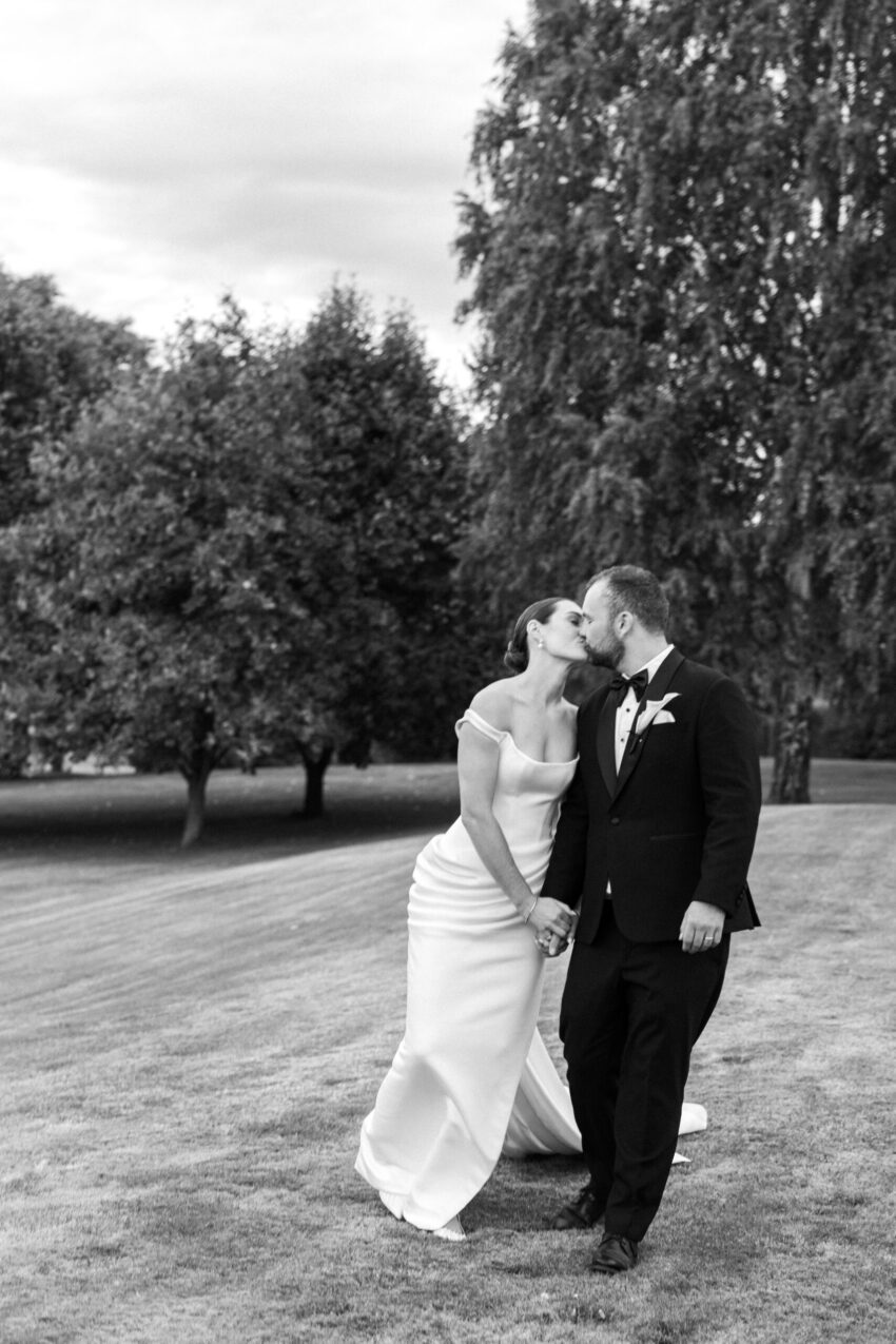 B&W of bride and groom walking along kissing