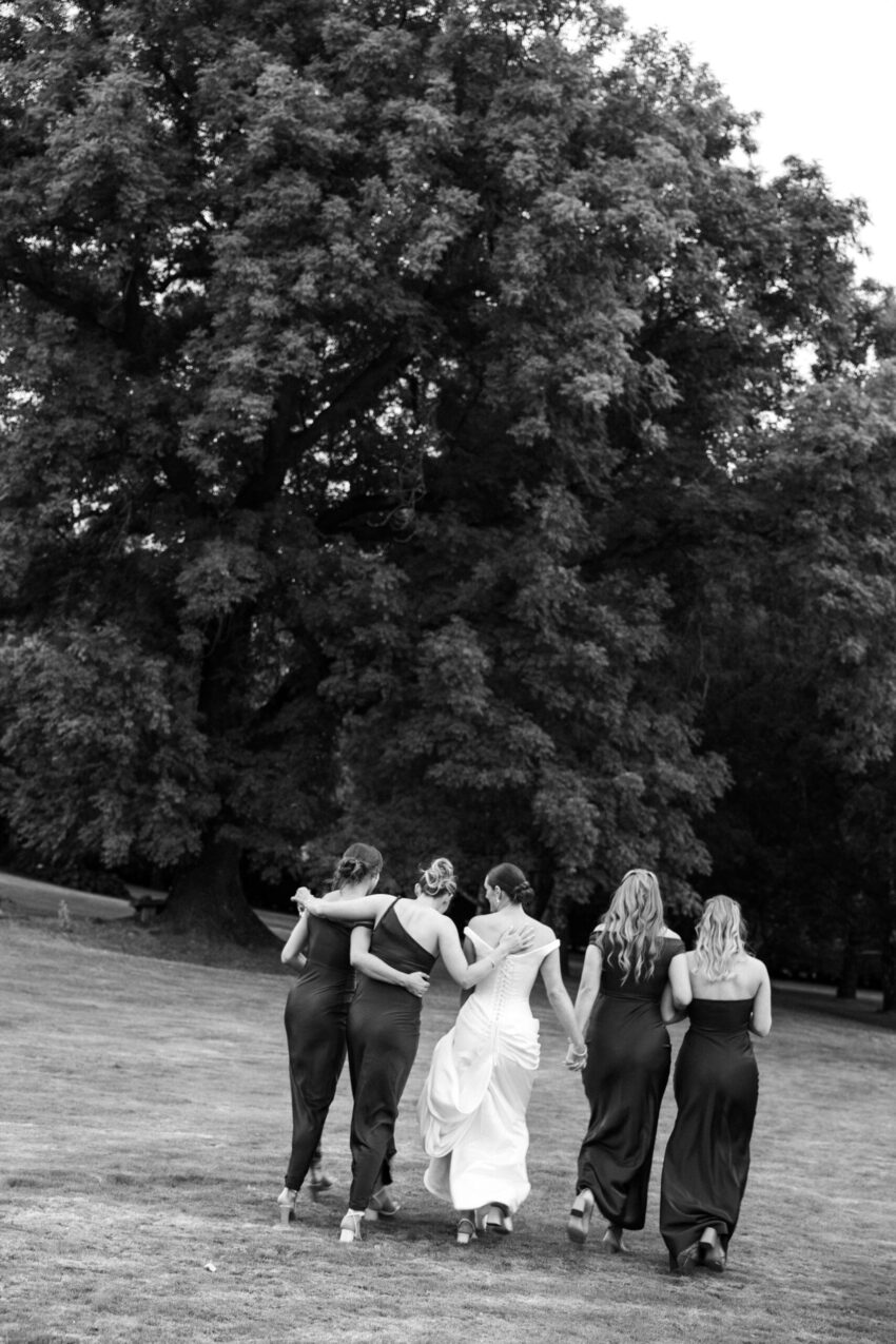 Bride and her 4 bridesmaids walking away sharing a cuddle and a moment B&W