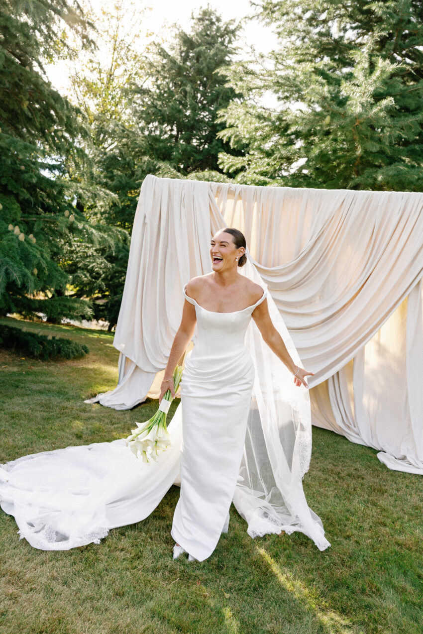 The bride laughing candidly with her flowers in hand in front of draping