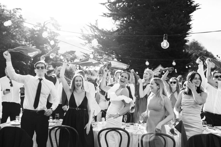 B&W shot of guests cheering and holding napkins in the air in excitement
