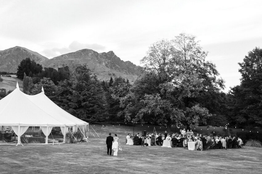 B&W shot from a distance of bride and groom rejoining the reception with mountain back drop