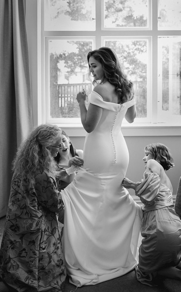 candid moment of bride being dressed by her mother and bridesmaids